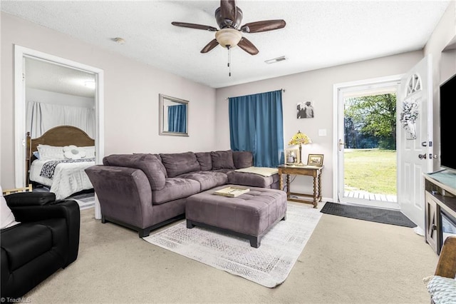carpeted living room featuring visible vents, a ceiling fan, and a textured ceiling