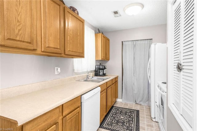 kitchen with visible vents, brown cabinetry, white appliances, light countertops, and a sink
