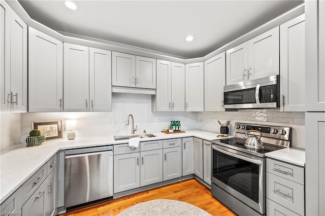 kitchen featuring sink, gray cabinetry, light hardwood / wood-style flooring, stainless steel appliances, and decorative backsplash