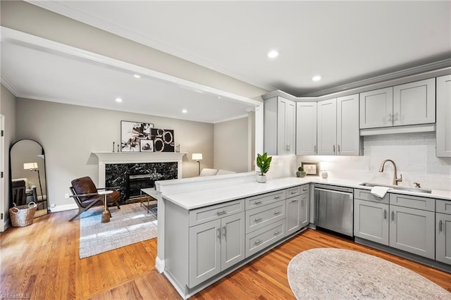 kitchen with light hardwood / wood-style floors, stainless steel dishwasher, kitchen peninsula, and sink