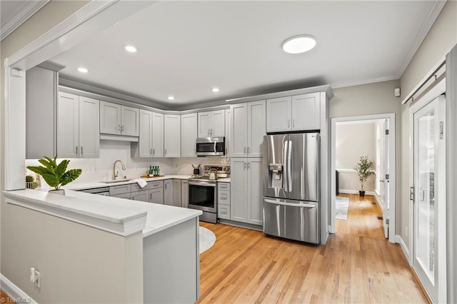 kitchen featuring crown molding, light hardwood / wood-style flooring, gray cabinets, stainless steel appliances, and kitchen peninsula