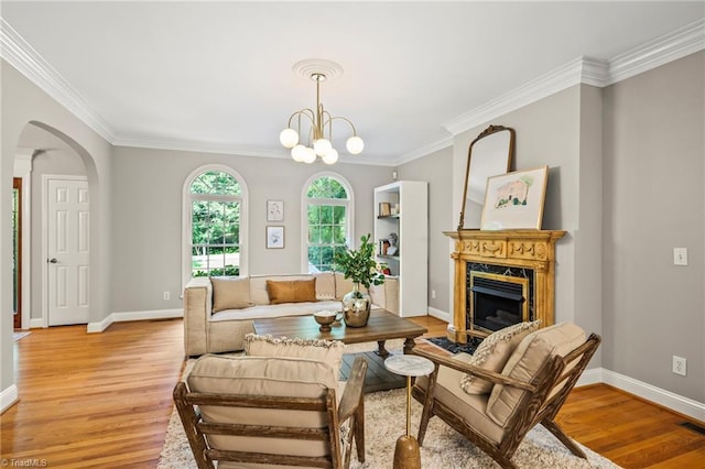 living room with an inviting chandelier, ornamental molding, a high end fireplace, and light wood-type flooring