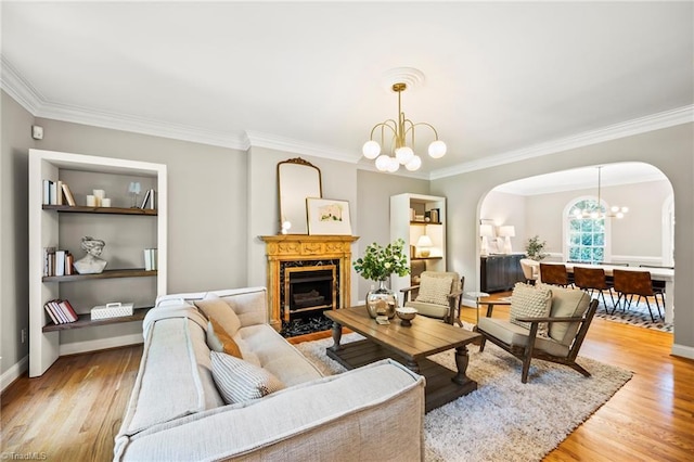 living room featuring a premium fireplace, ornamental molding, an inviting chandelier, and light hardwood / wood-style floors