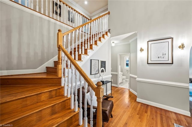 stairway with ornamental molding, wood-type flooring, and a towering ceiling