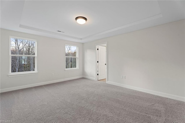 empty room with carpet floors, visible vents, a tray ceiling, and baseboards