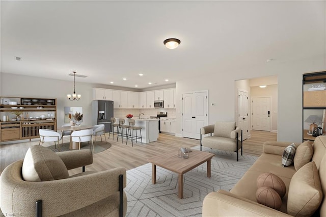 living area with light wood finished floors, recessed lighting, and an inviting chandelier