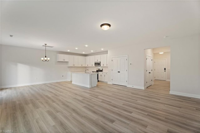 unfurnished living room featuring baseboards, light wood-style flooring, an inviting chandelier, a sink, and recessed lighting