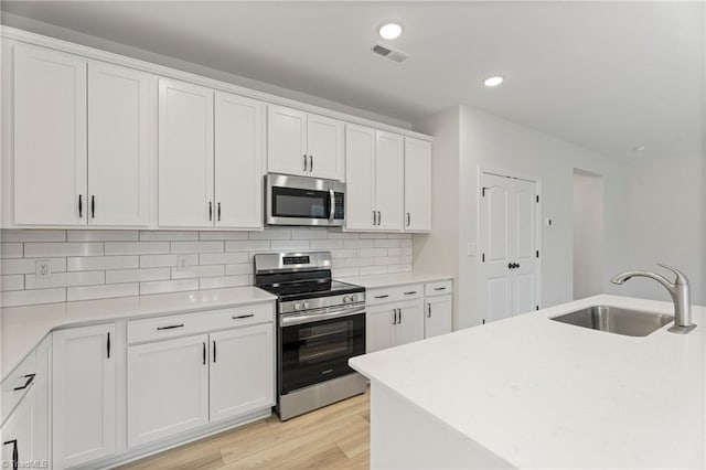 kitchen featuring tasteful backsplash, appliances with stainless steel finishes, light wood-type flooring, white cabinetry, and a sink