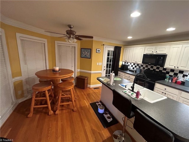 kitchen featuring ceiling fan, tasteful backsplash, light wood-type flooring, black appliances, and ornamental molding