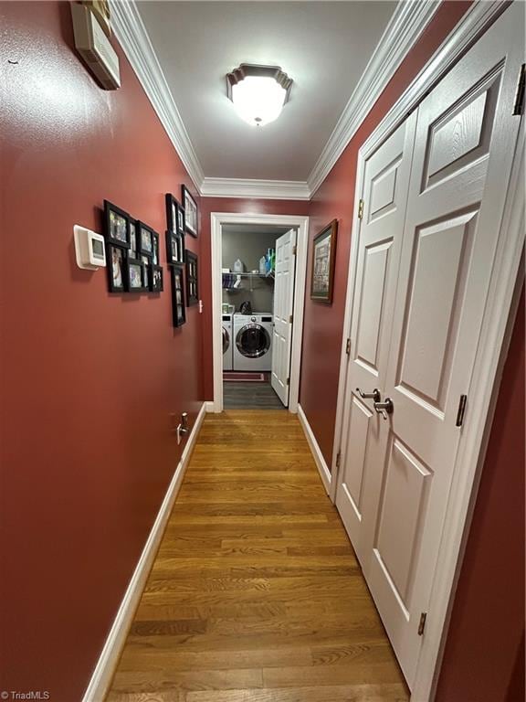 hallway with wood-type flooring, ornamental molding, and washing machine and clothes dryer