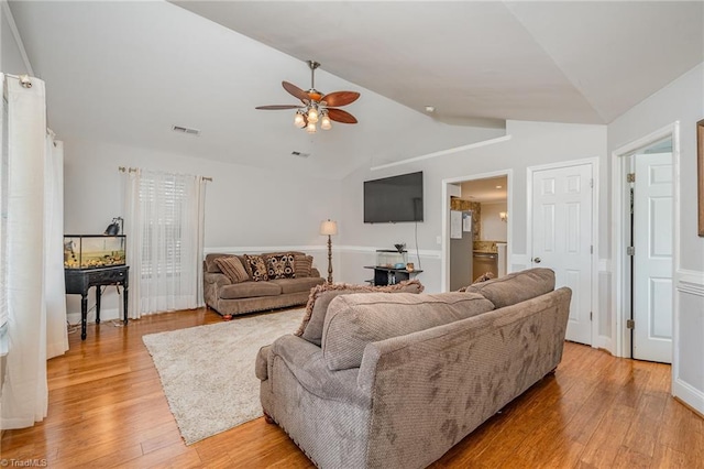 living room with ceiling fan, light hardwood / wood-style floors, and vaulted ceiling