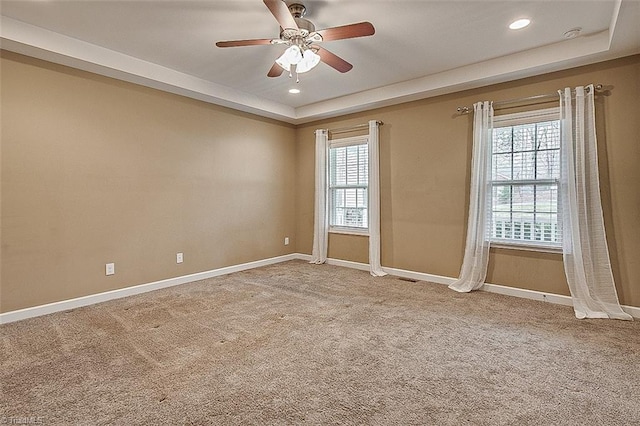 carpeted spare room featuring a tray ceiling, baseboards, a healthy amount of sunlight, and ceiling fan