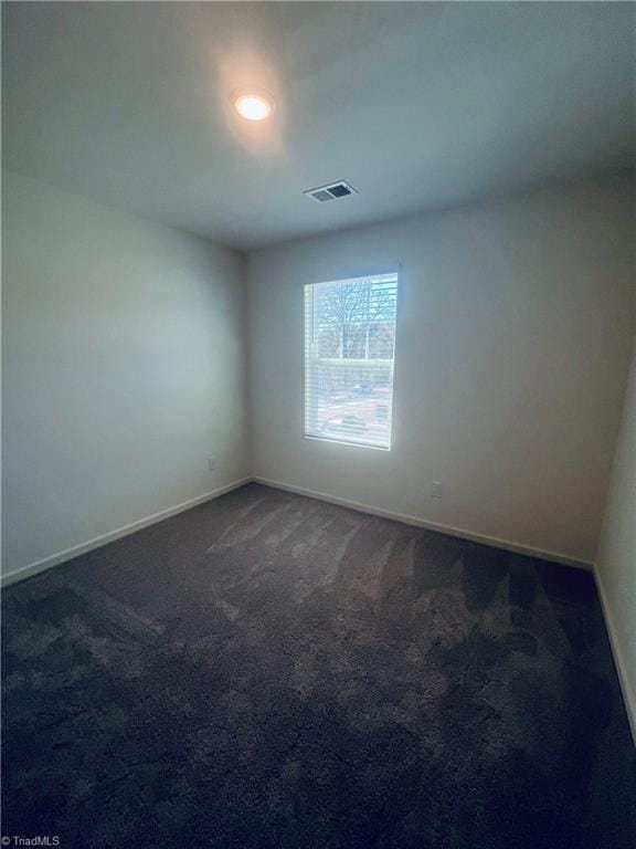 empty room with baseboards, dark colored carpet, and visible vents