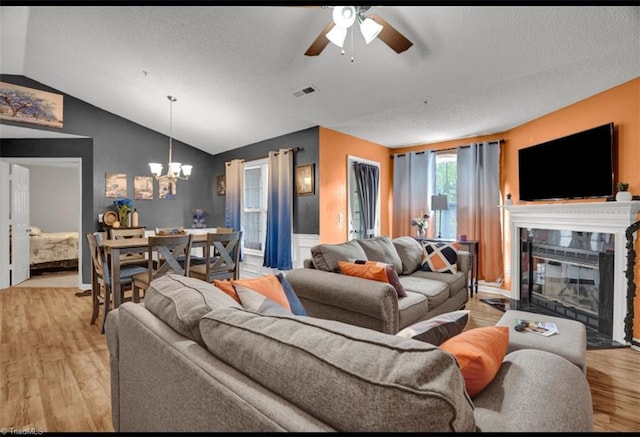 living room with a textured ceiling, ceiling fan with notable chandelier, light hardwood / wood-style floors, and vaulted ceiling