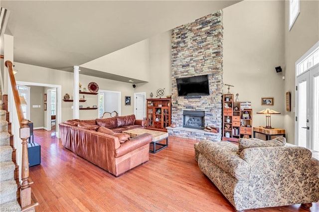 living room with a stone fireplace, wood finished floors, a towering ceiling, stairs, and ornate columns