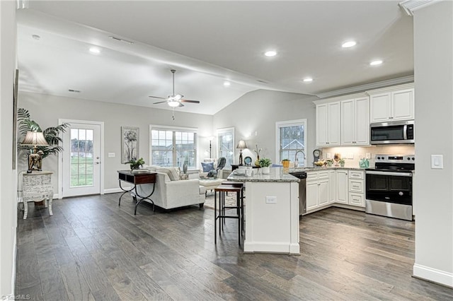 kitchen featuring a breakfast bar area, white cabinets, lofted ceiling, stainless steel appliances, and light stone countertops