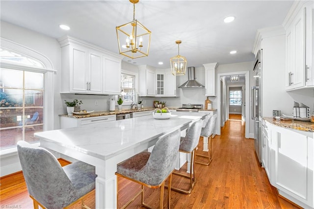 kitchen featuring white cabinetry, wall chimney exhaust hood, pendant lighting, and a kitchen island