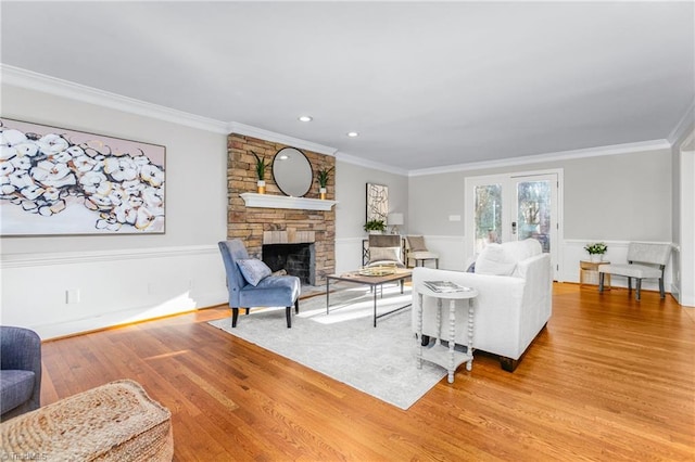 living room featuring a stone fireplace, ornamental molding, french doors, and light hardwood / wood-style flooring