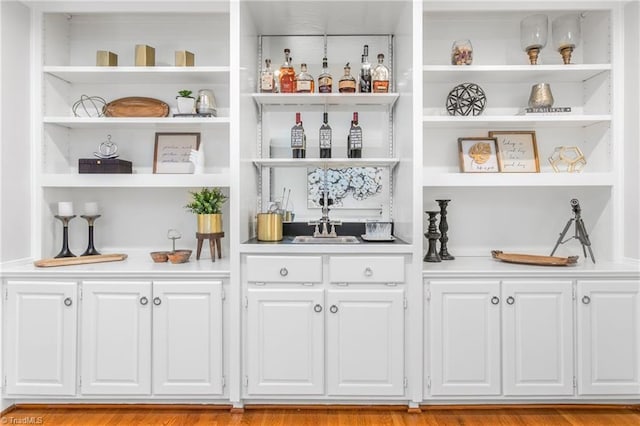 bar with light wood-type flooring and white cabinetry