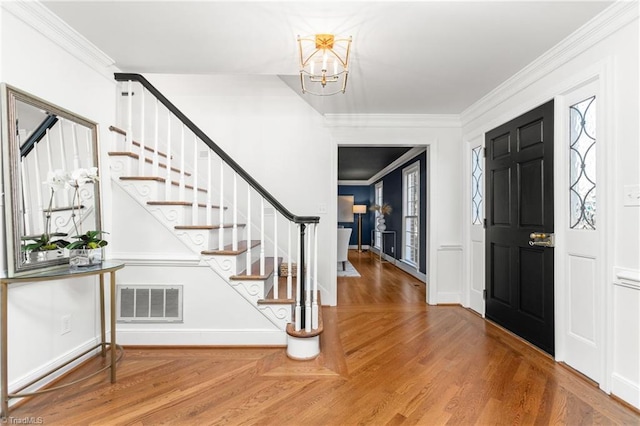 foyer entrance with wood-type flooring, ornamental molding, and a chandelier