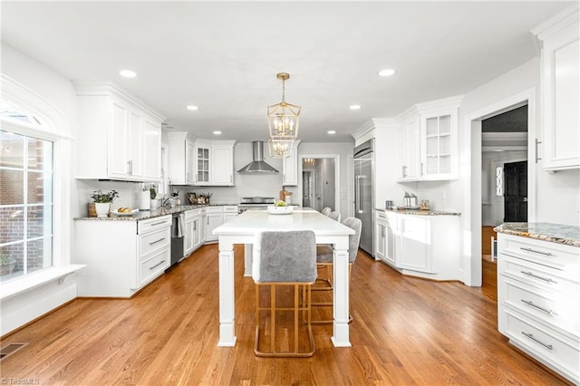 kitchen featuring appliances with stainless steel finishes, white cabinetry, a kitchen island, and wall chimney range hood