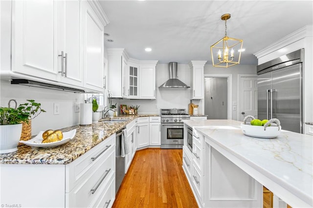 kitchen featuring white cabinetry, wall chimney exhaust hood, an inviting chandelier, built in appliances, and pendant lighting