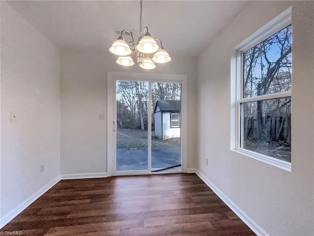 unfurnished dining area featuring plenty of natural light, dark wood-type flooring, and an inviting chandelier