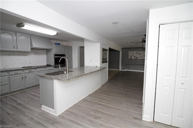 kitchen featuring a sink, custom exhaust hood, ceiling fan, light stone counters, and a peninsula