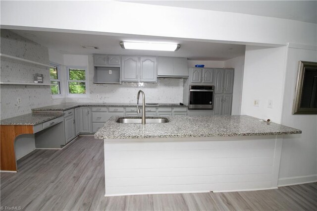 kitchen with stainless steel oven, a sink, light stone countertops, and light wood-style floors