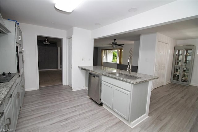 kitchen featuring appliances with stainless steel finishes, a sink, a ceiling fan, light wood finished floors, and light stone counters