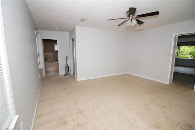 unfurnished room featuring light colored carpet, a ceiling fan, a textured ceiling, and baseboards