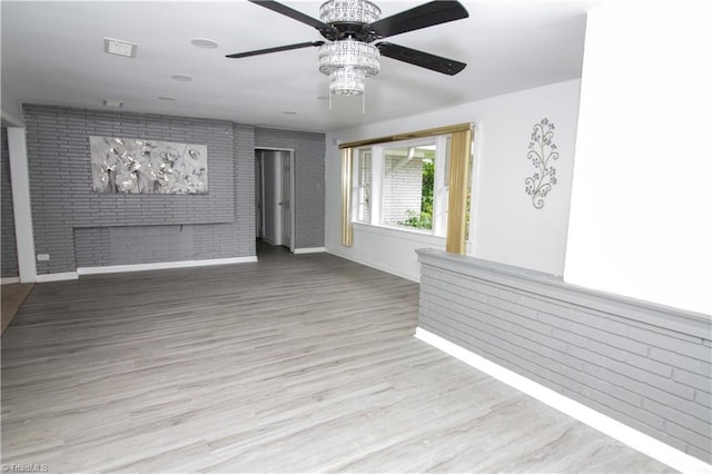 spare room featuring a ceiling fan, brick wall, wood finished floors, and baseboards