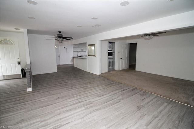 unfurnished living room with a ceiling fan, wood finished floors, and a sink