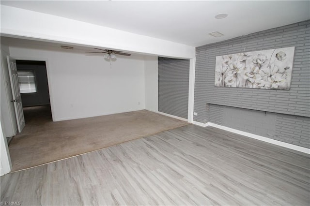 below grade area with a ceiling fan, wood finished floors, baseboards, and brick wall