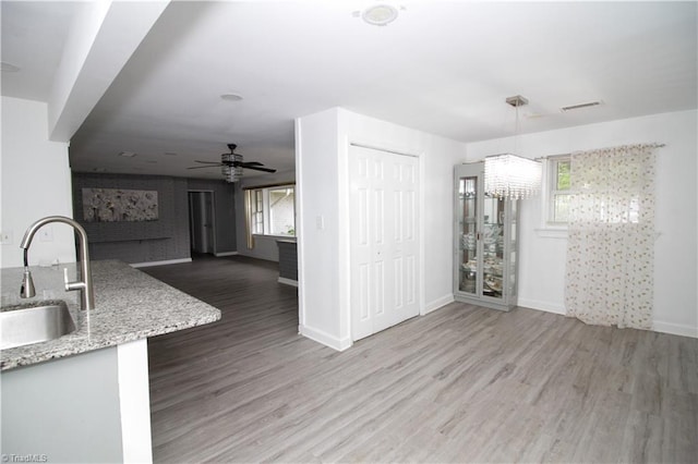 unfurnished living room featuring a sink, wood finished floors, baseboards, a ceiling fan, and a chandelier