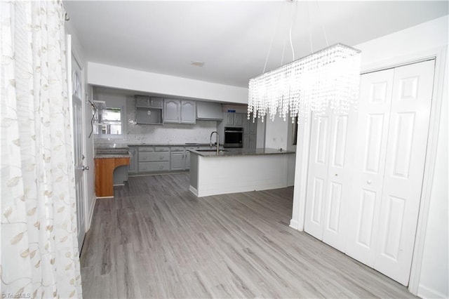 kitchen featuring oven, gray cabinetry, wood finished floors, a chandelier, and a peninsula