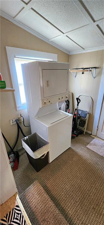 laundry room featuring stacked washer / dryer, tile patterned floors, and crown molding