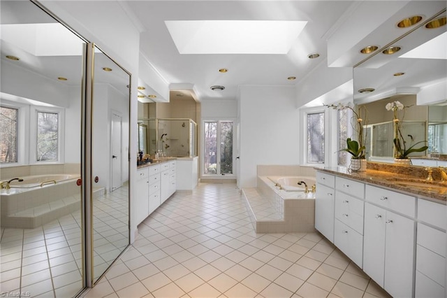 bathroom with a skylight, two vanities, a stall shower, a sink, and a bath