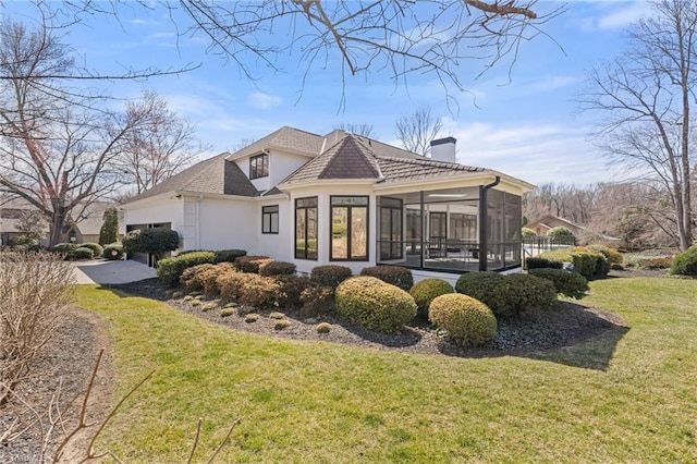 exterior space with a yard, a chimney, stucco siding, a sunroom, and a garage