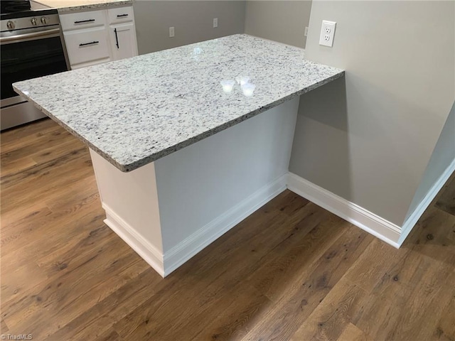 kitchen with hardwood / wood-style flooring, light stone countertops, stainless steel electric range, and white cabinets