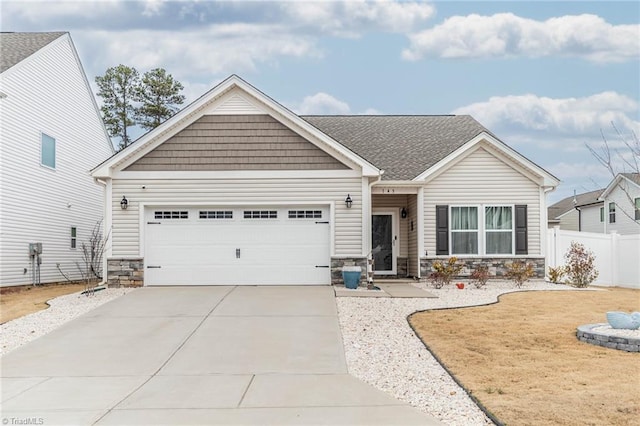 view of front facade featuring a garage, a shingled roof, concrete driveway, stone siding, and fence