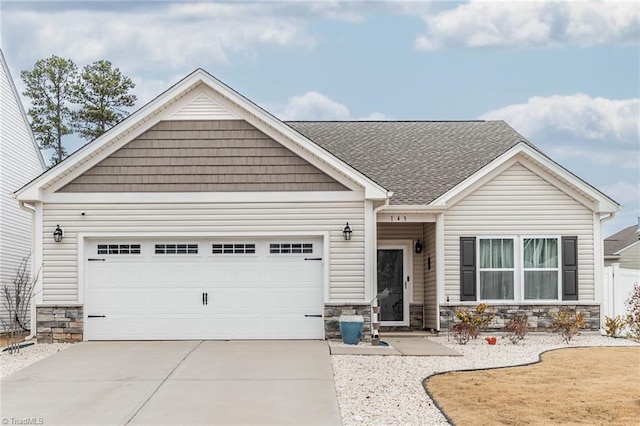 view of front of home featuring driveway, a garage, stone siding, roof with shingles, and fence