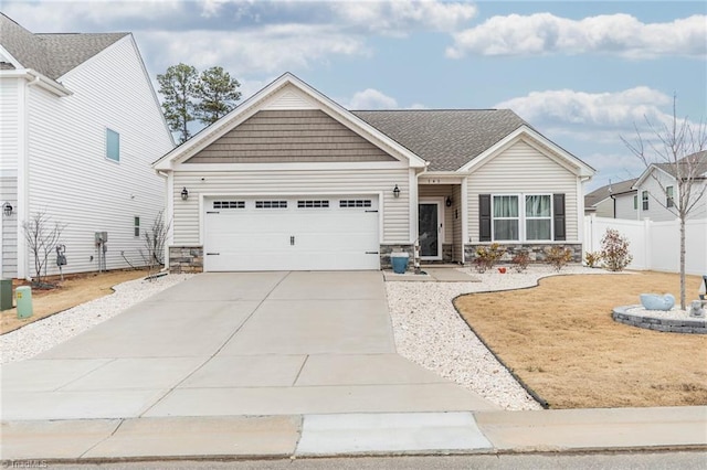 view of front of house featuring driveway, stone siding, an attached garage, and fence