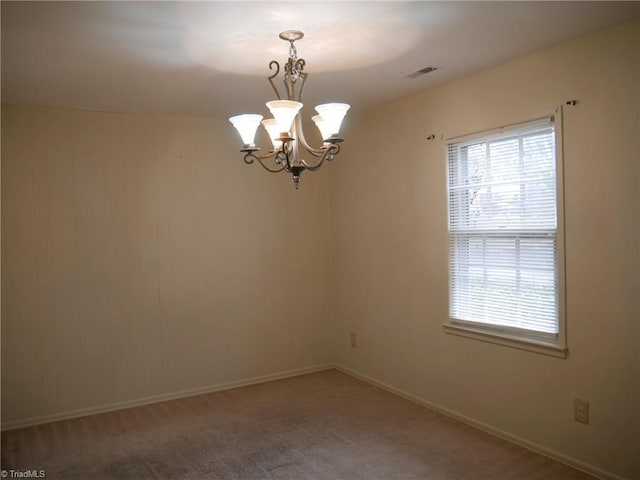 carpeted spare room featuring a chandelier