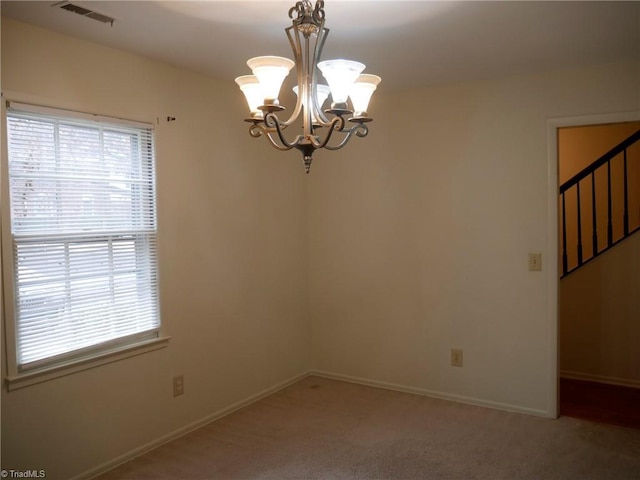 carpeted spare room featuring an inviting chandelier