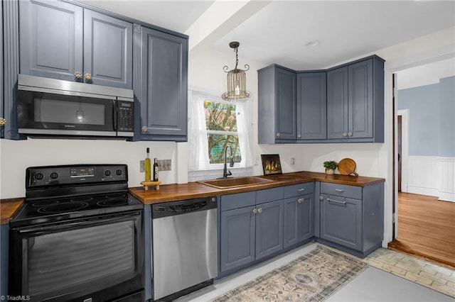 kitchen with pendant lighting, butcher block countertops, stainless steel appliances, and sink