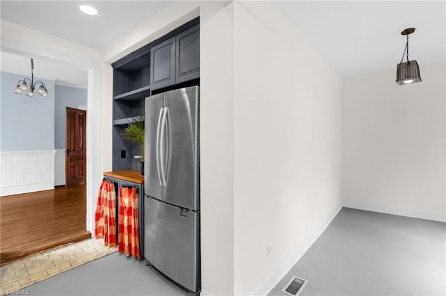 kitchen featuring wood counters, concrete flooring, an inviting chandelier, decorative light fixtures, and stainless steel refrigerator