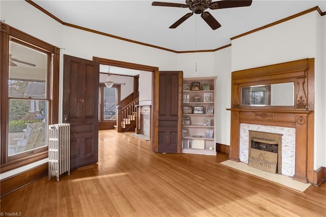 unfurnished living room with hardwood / wood-style flooring, ceiling fan, radiator heating unit, and crown molding