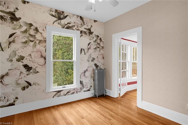 spare room featuring a healthy amount of sunlight, radiator heating unit, and light wood-type flooring