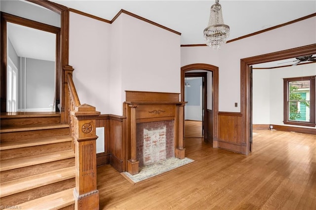 unfurnished living room featuring crown molding, wooden walls, ceiling fan with notable chandelier, and light hardwood / wood-style flooring